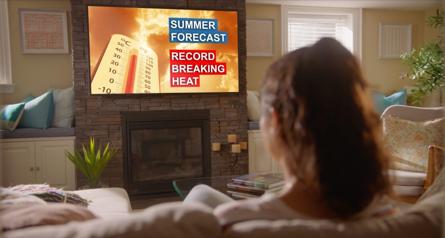 woman sitting in living room and watching tv with a forecast that says hot weather is coming